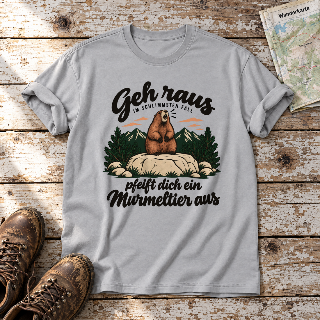 Pfeift dich ein Murmeltier aus – T-Shirt Unisex in Hellgrau, flach liegend auf alten Holzbrettern mit Wanderschuhen und Wanderkarte.