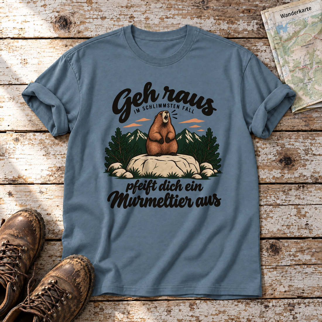 Pfeift dich ein Murmeltier aus – T-Shirt Unisex in Steinblau, flach liegend auf alten Holzbrettern mit Wanderschuhen und Wanderkarte.