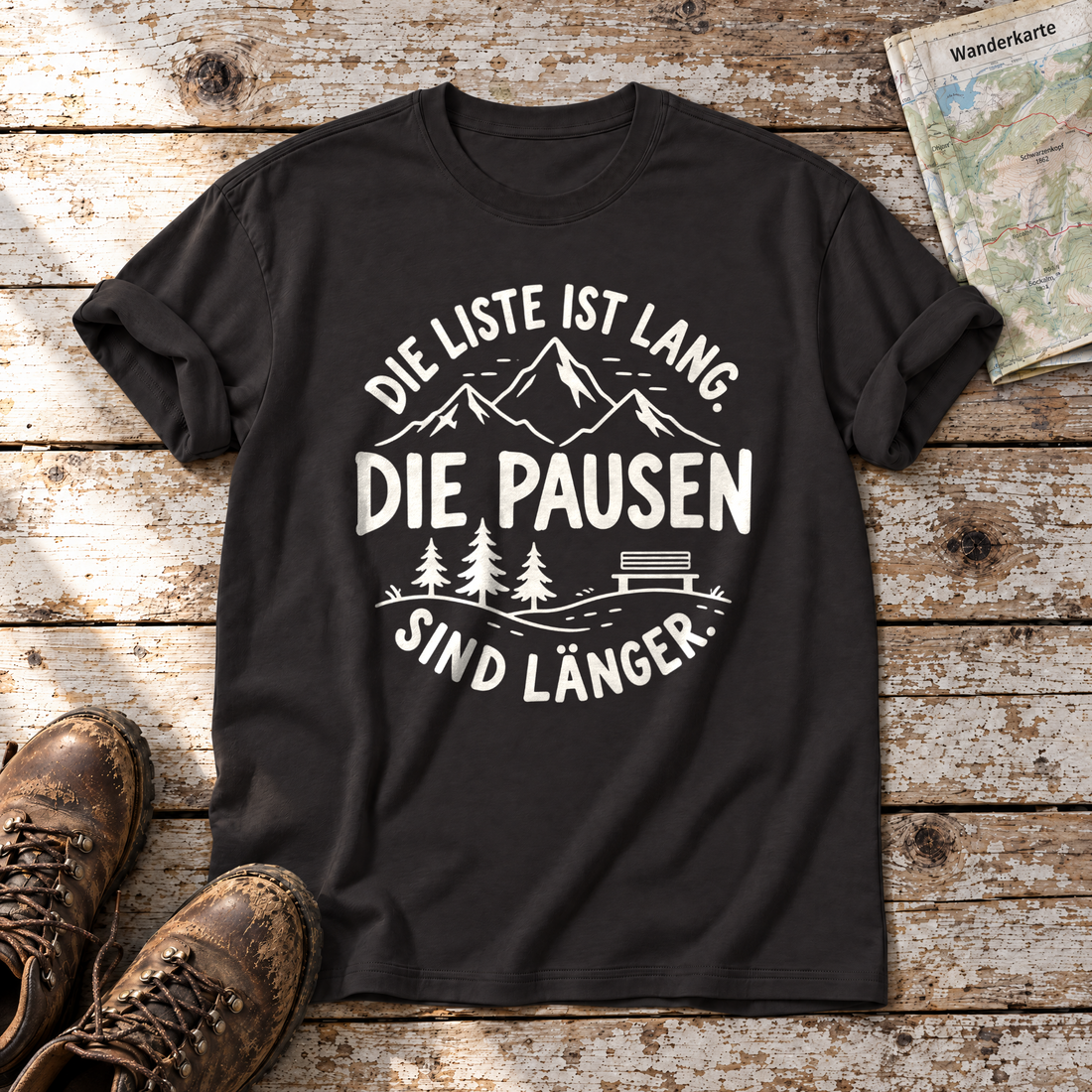 Die Pausen sind länger – T-Shirt Unisex in Schwarz, flach liegend auf alten Holzbrettern mit Wanderschuhen und Wanderkarte.