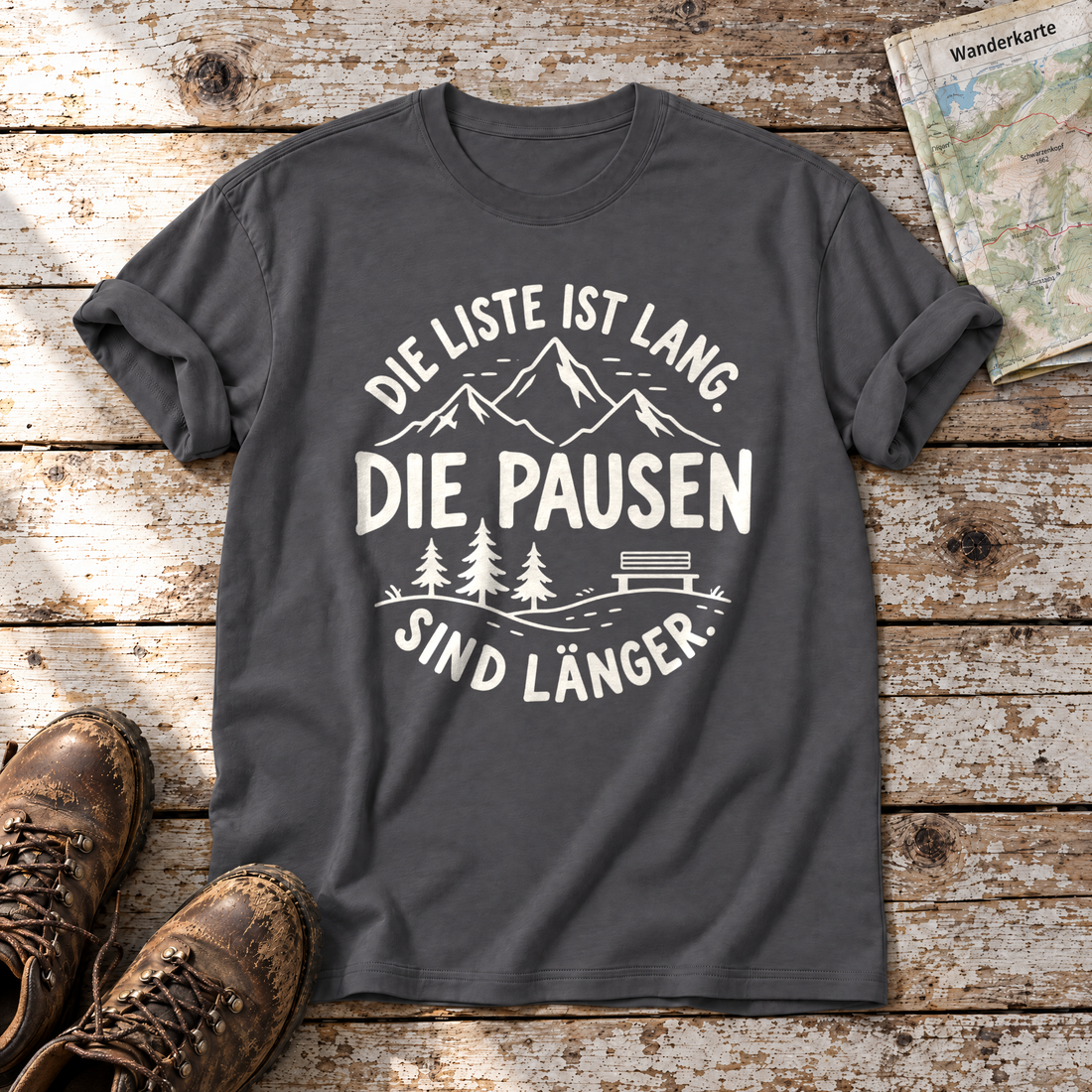 Die Pausen sind länger – T-Shirt Unisex in Dunkelgrau, flach liegend auf alten Holzbrettern mit Wanderschuhen und Wanderkarte.