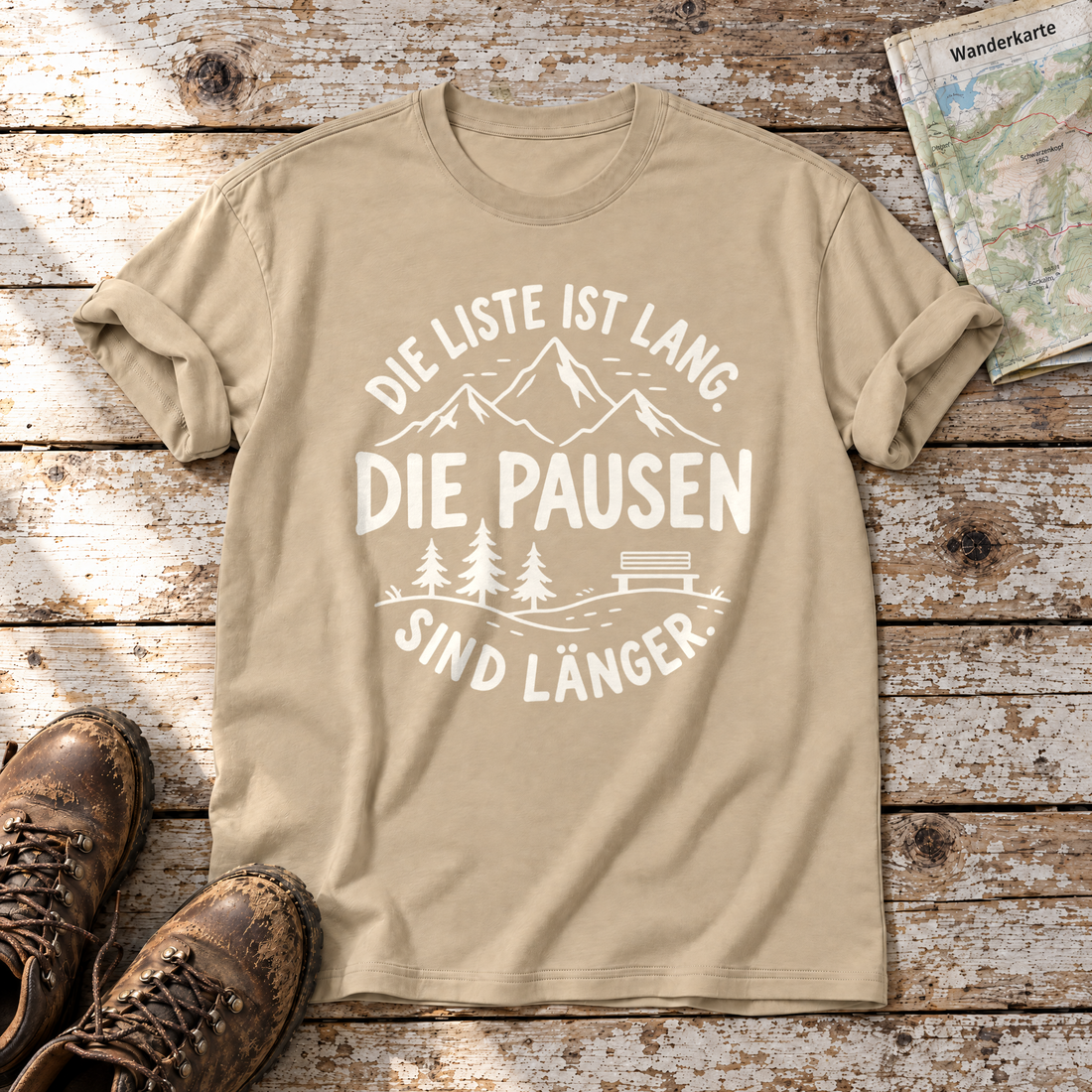 Die Pausen sind länger – T-Shirt Unisex in Sand, flach liegend auf alten Holzbrettern mit Wanderschuhen und Wanderkarte.
