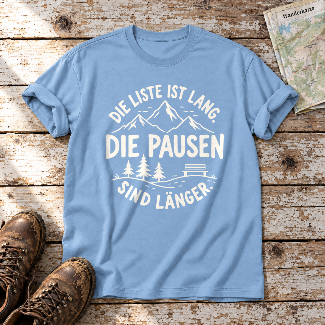 Die Pausen sind länger – T-Shirt Unisex in Himmelblau, flach liegend auf alten Holzbrettern mit Wanderschuhen und Wanderkarte.