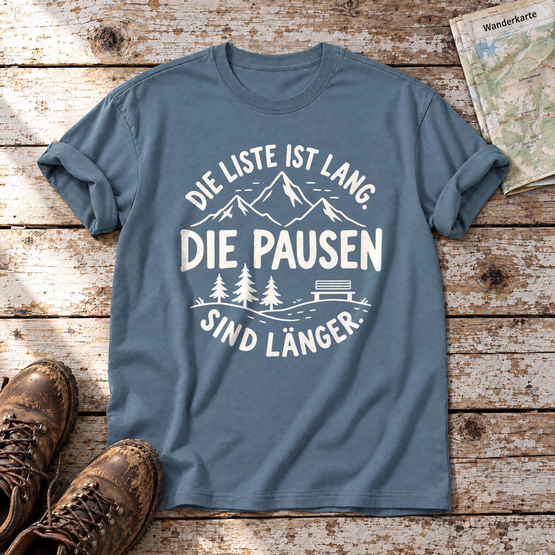 Die Pausen sind länger – T-Shirt Unisex in Steinblau, flach liegend auf alten Holzbrettern mit Wanderschuhen und Wanderkarte.