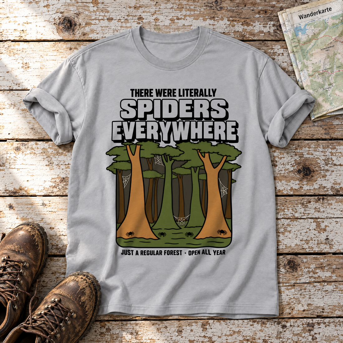 Literally Spiders Everywhere – T-Shirt Unisex in Hellgrau, flach liegend auf alten Holzbrettern mit Wanderschuhen und Wanderkarte.