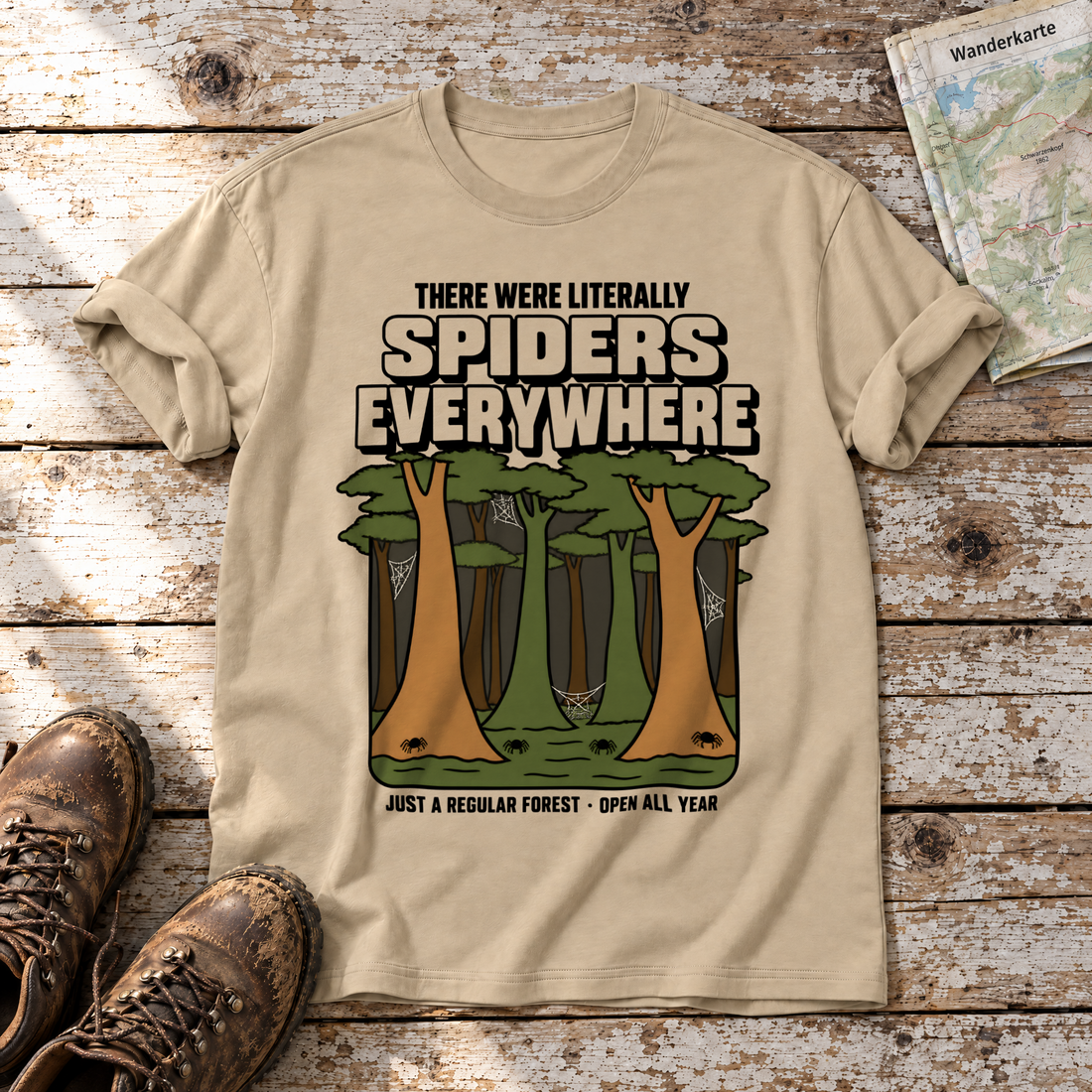 Literally Spiders Everywhere – T-Shirt Unisex in Sand, flach liegend auf alten Holzbrettern mit Wanderschuhen und Wanderkarte.