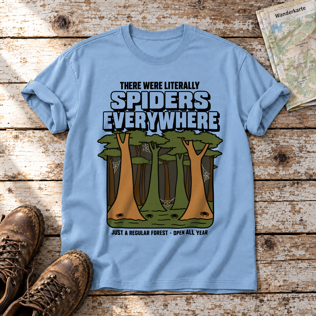 Literally Spiders Everywhere – T-Shirt Unisex in Himmelblau, flach liegend auf alten Holzbrettern mit Wanderschuhen und Wanderkarte.