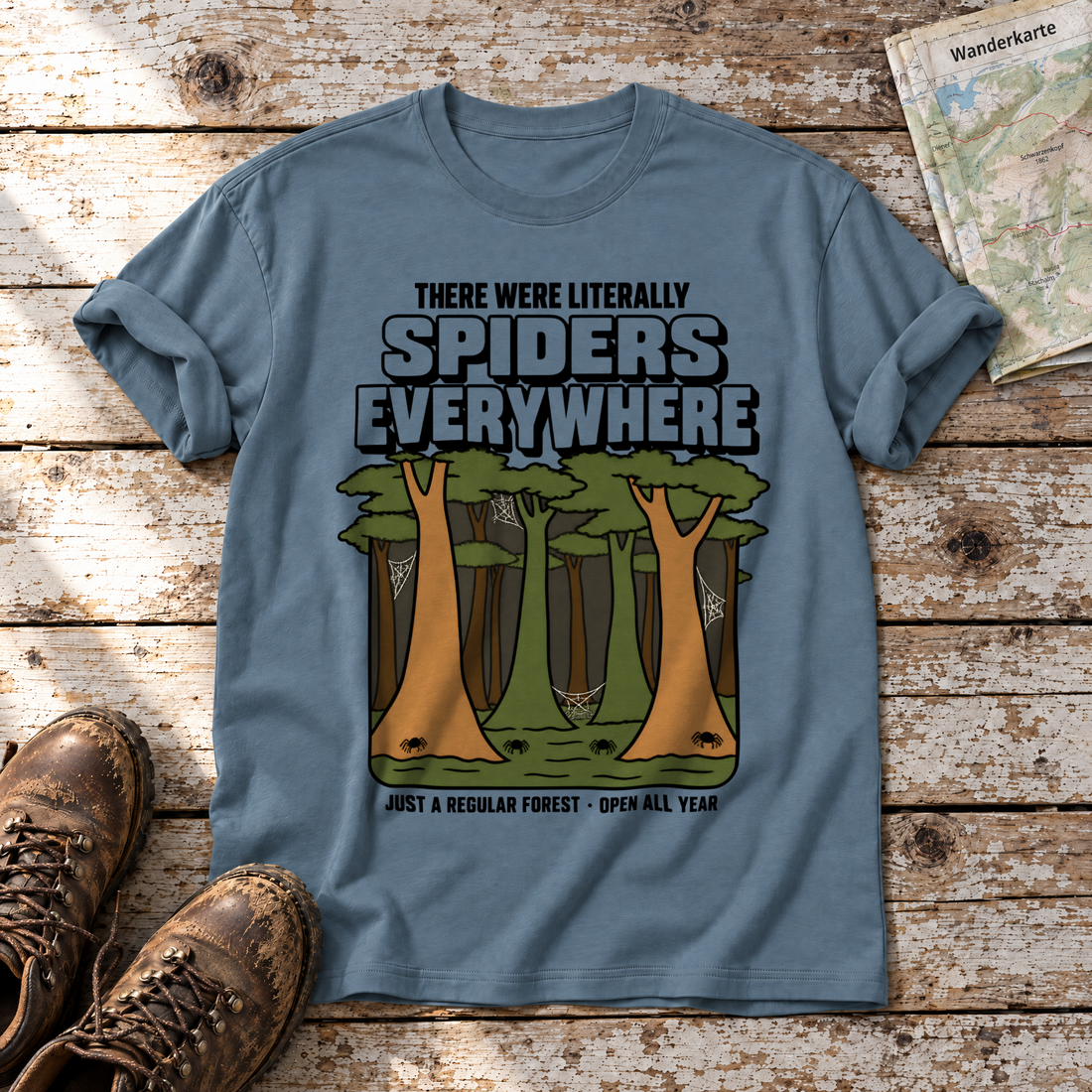 Literally Spiders Everywhere – T-Shirt Unisex in Steinblau, flach liegend auf alten Holzbrettern mit Wanderschuhen und Wanderkarte.