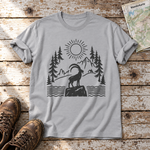 Steinbock am Bergsee – T-Shirt Unisex in Hellgrau, flach liegend auf alten Holzbrettern mit Wanderschuhen und Wanderkarte.