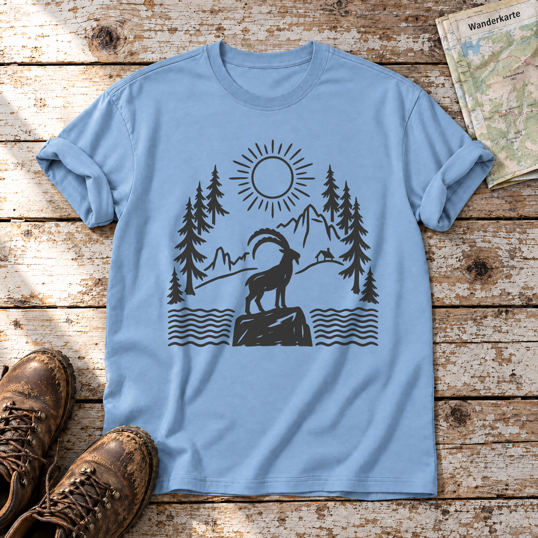 Steinbock am Bergsee – T-Shirt Unisex in Himmelblau, flach liegend auf alten Holzbrettern mit Wanderschuhen und Wanderkarte.