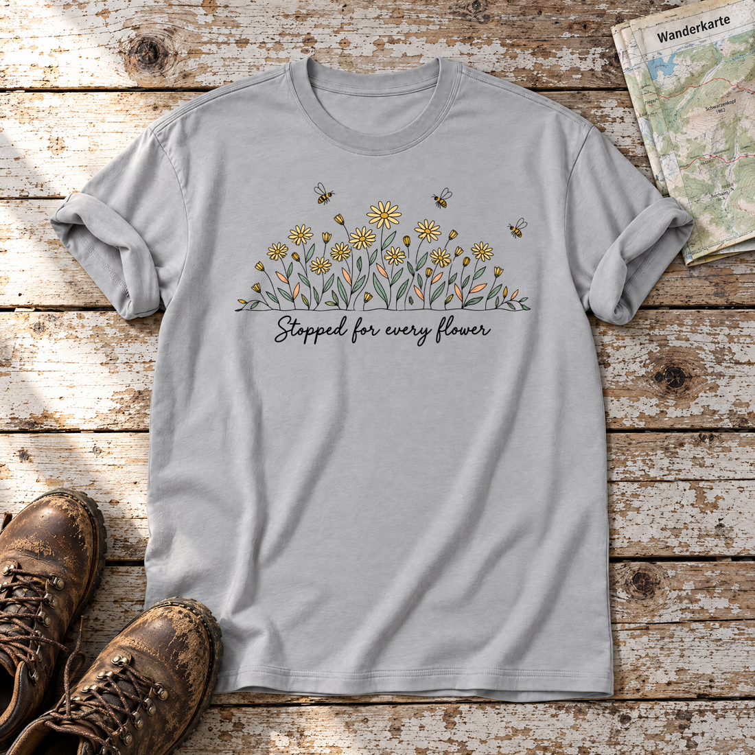 Stopped for every flower – T-Shirt Unisex in Hellgrau, flach liegend auf alten Holzbrettern mit Wanderschuhen und Wanderkarte.