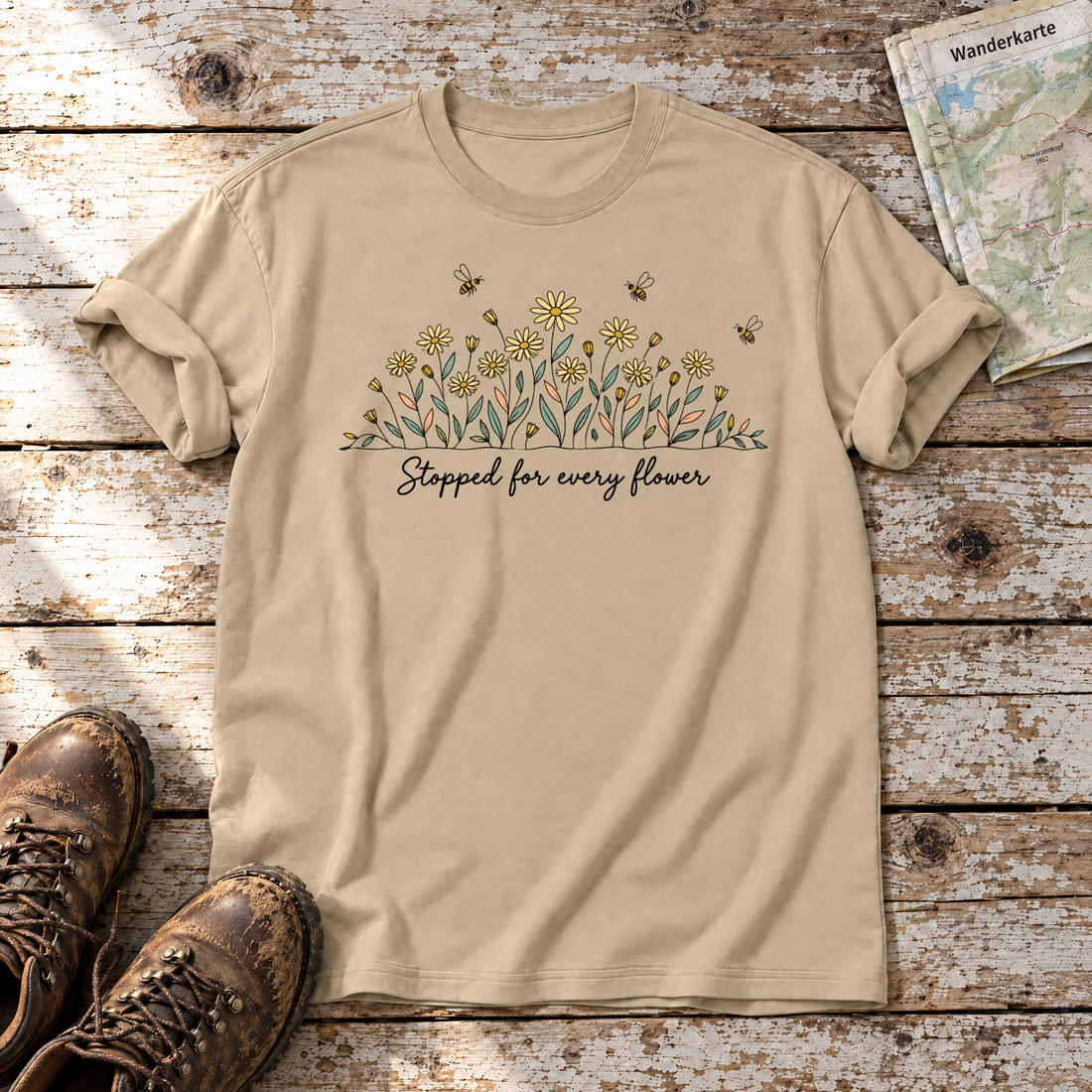 Stopped for every flower – T-Shirt Unisex in Sand, flach liegend auf alten Holzbrettern mit Wanderschuhen und Wanderkarte.