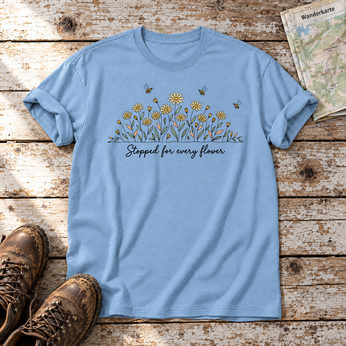 Stopped for every flower – T-Shirt Unisex in Himmelblau, flach liegend auf alten Holzbrettern mit Wanderschuhen und Wanderkarte.