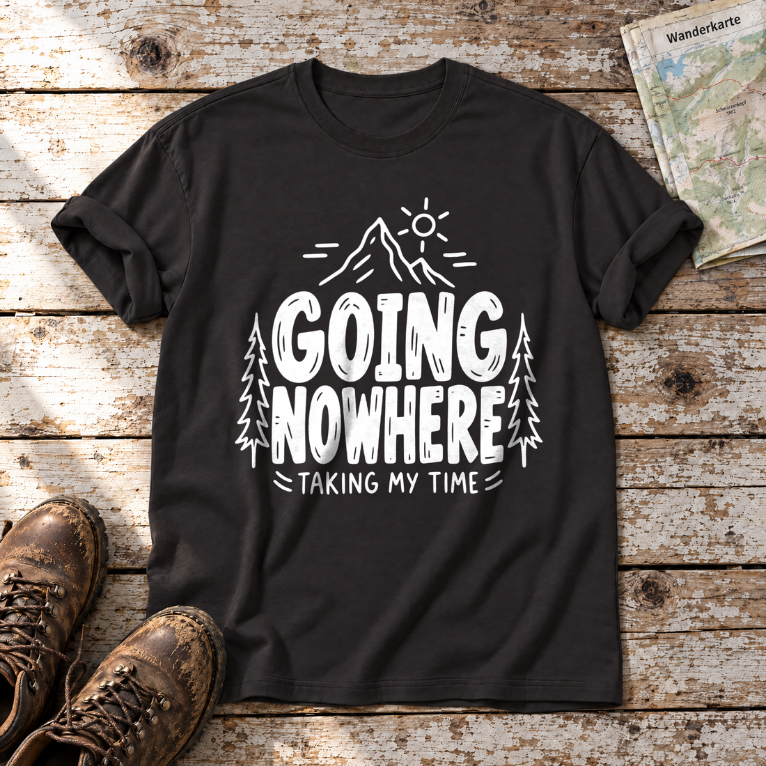 Going Nowhere – T-Shirt Unisex in Schwarz, flach liegend auf alten Holzbrettern mit Wanderschuhen und Wanderkarte.