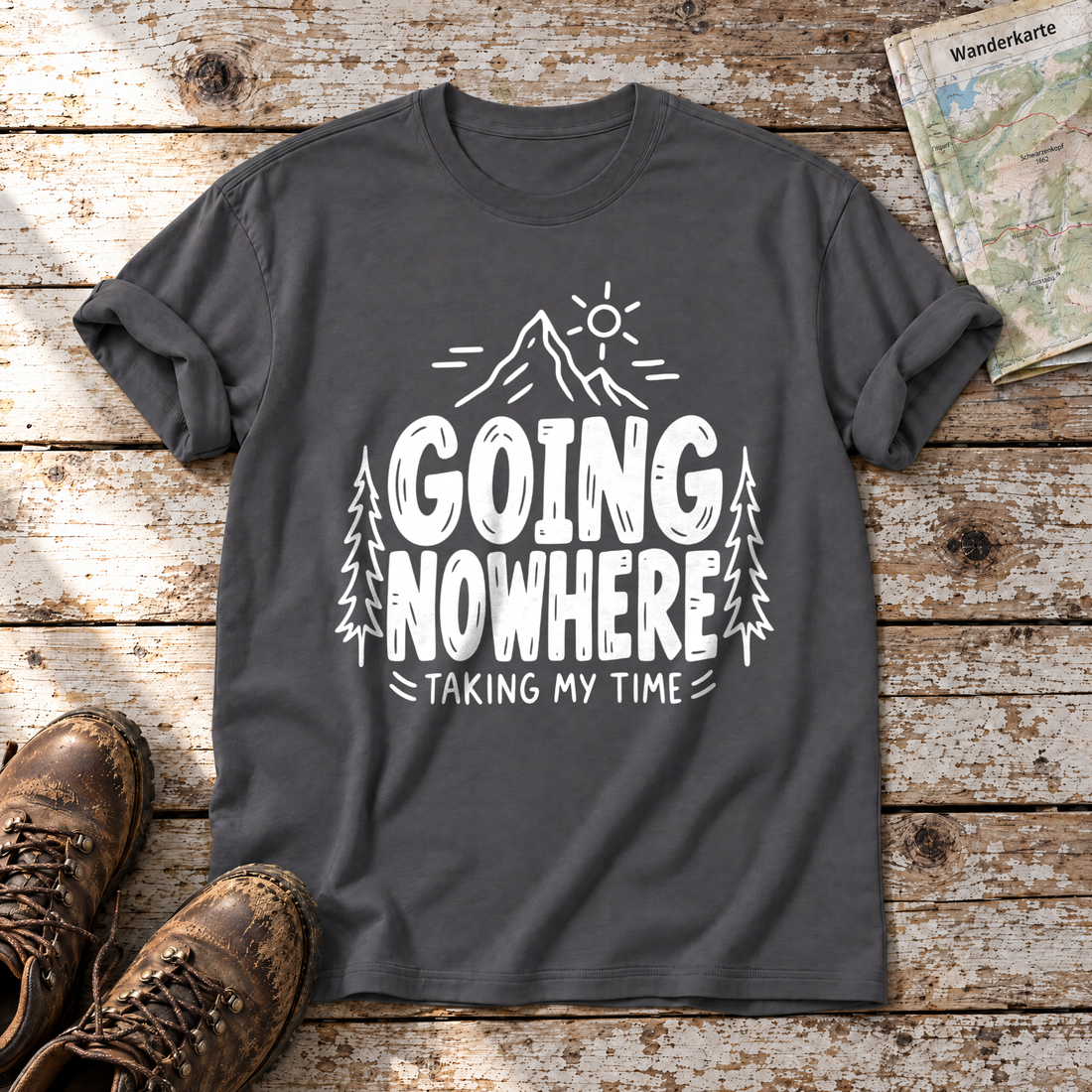 Going Nowhere – T-Shirt Unisex in Dunkelgrau, flach liegend auf alten Holzbrettern mit Wanderschuhen und Wanderkarte.