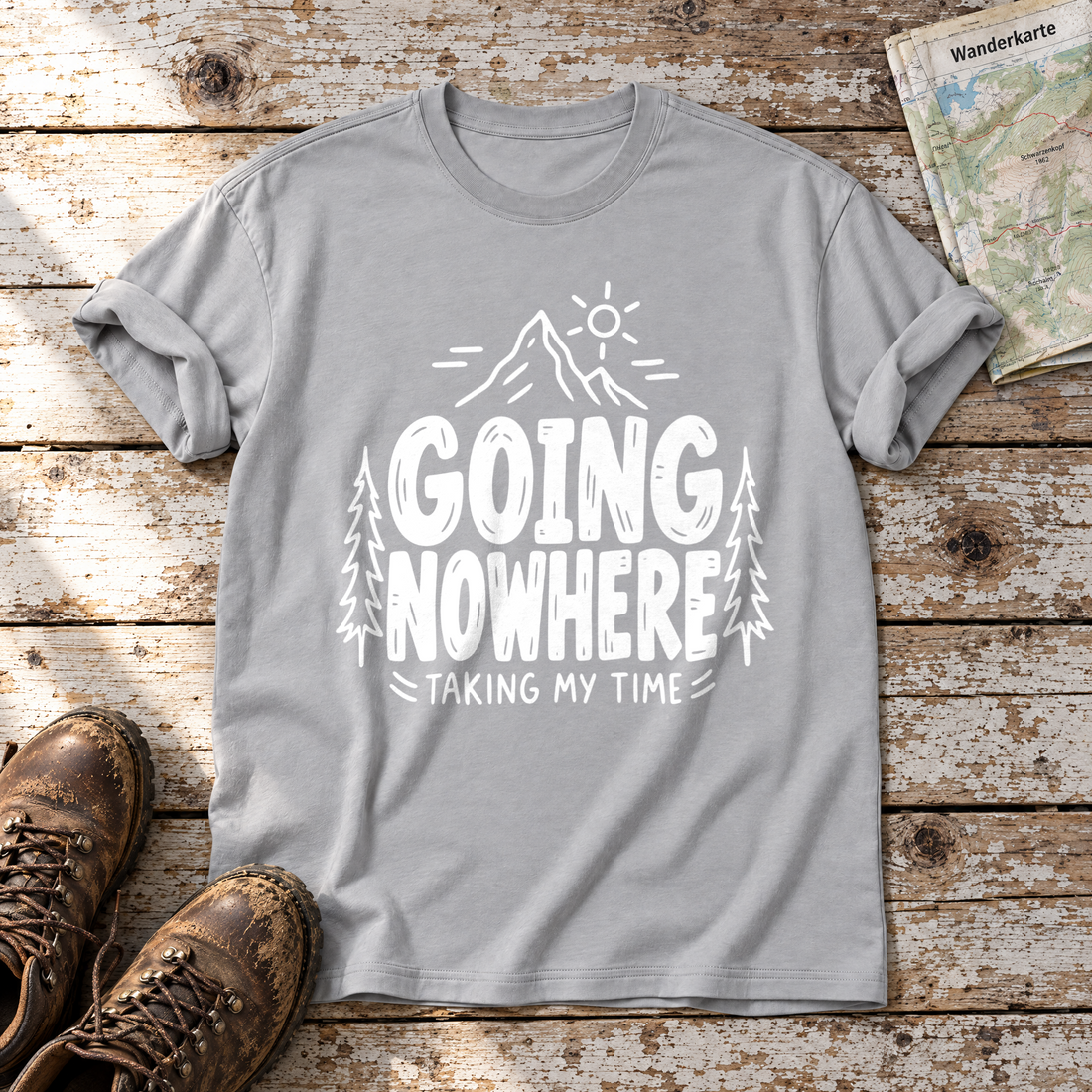 Going Nowhere – T-Shirt Unisex in Hellgrau, flach liegend auf alten Holzbrettern mit Wanderschuhen und Wanderkarte.