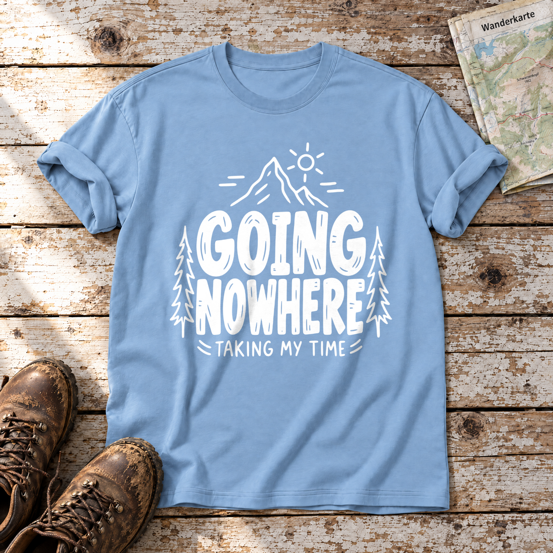 Going Nowhere – T-Shirt Unisex in Himmelblau, flach liegend auf alten Holzbrettern mit Wanderschuhen und Wanderkarte.