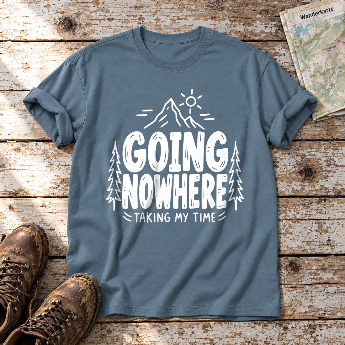 Going Nowhere – T-Shirt Unisex in Steinblau, flach liegend auf alten Holzbrettern mit Wanderschuhen und Wanderkarte.