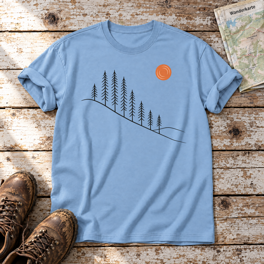 Tannenhang – T-Shirt Unisex in Himmelblau, flach liegend auf alten Holzbrettern mit Wanderschuhen und Wanderkarte.