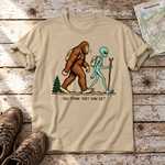 Think they saw us? – T-Shirt Unisex in Sand, flach liegend auf alten Holzbrettern mit Wanderschuhen und Wanderkarte.