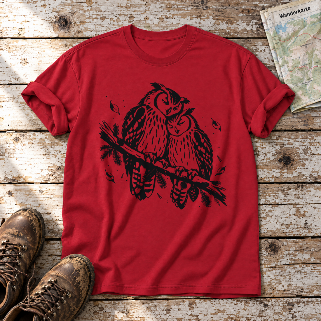 Uhupaar auf dem Fichtenast – T-Shirt Unisex in Rot, flach liegend auf alten Holzbrettern mit Wanderschuhen und Wanderkarte.