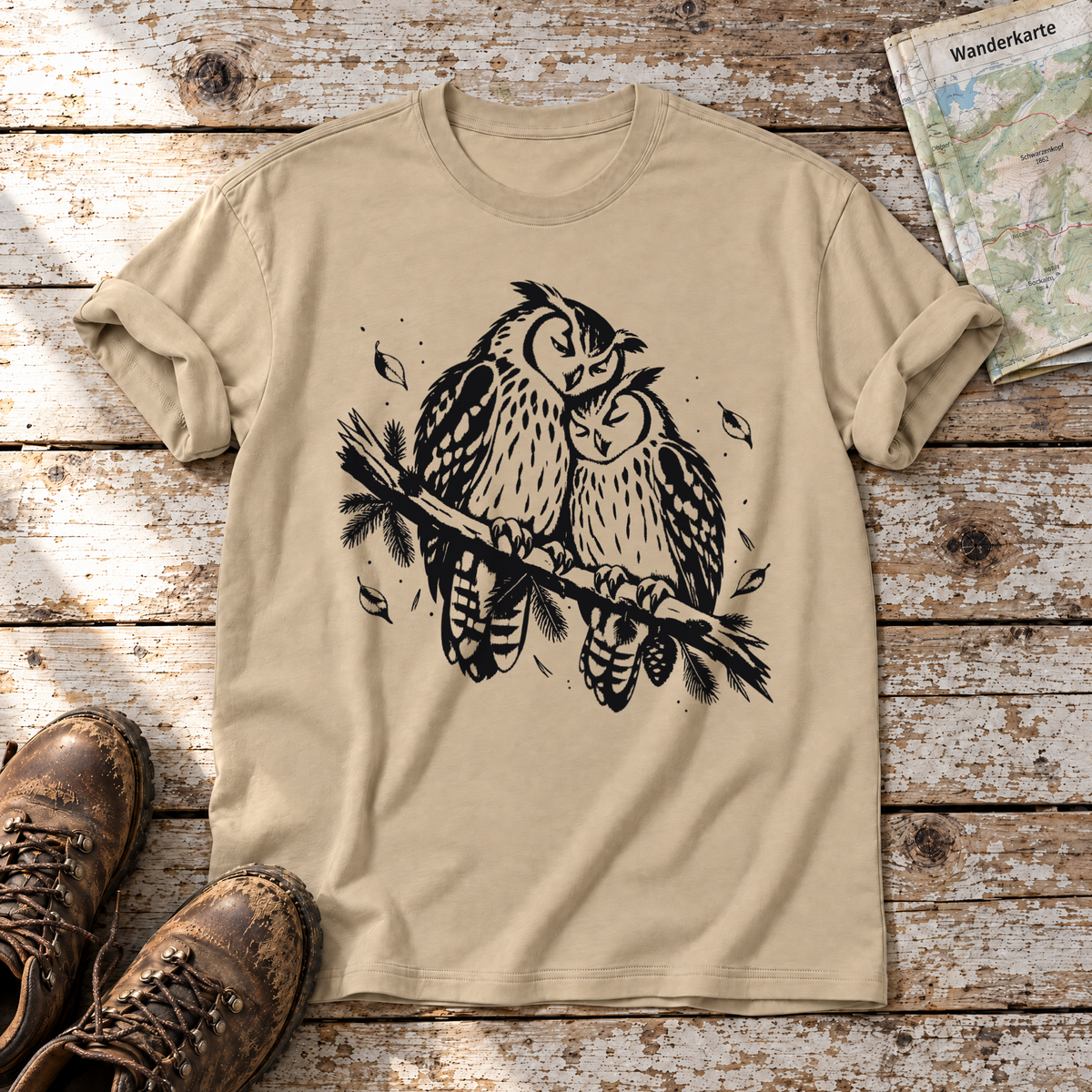 Uhupaar auf dem Fichtenast – T-Shirt Unisex in Sand, flach liegend auf alten Holzbrettern mit Wanderschuhen und Wanderkarte.
