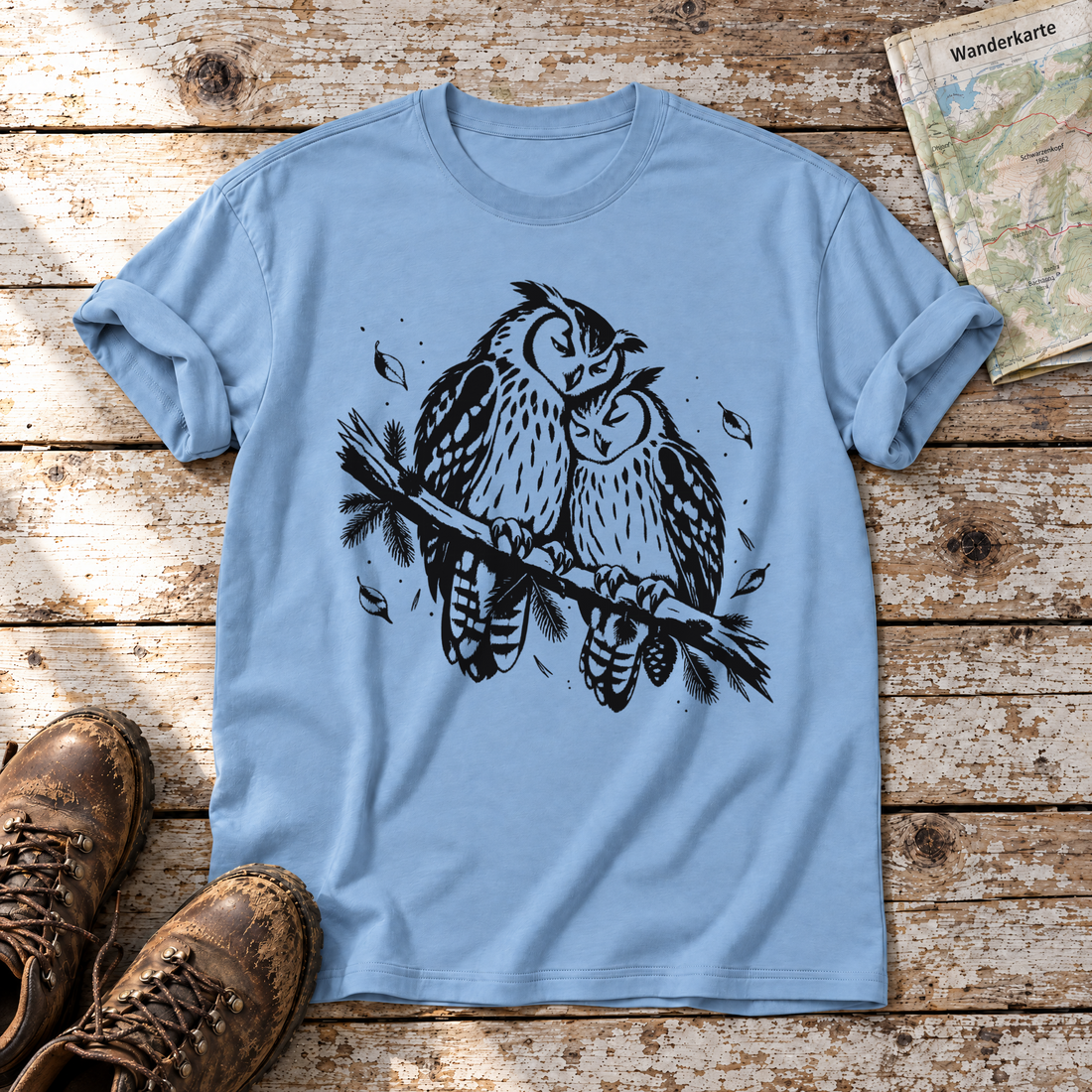 Uhupaar auf dem Fichtenast – T-Shirt Unisex in Himmelblau, flach liegend auf alten Holzbrettern mit Wanderschuhen und Wanderkarte.