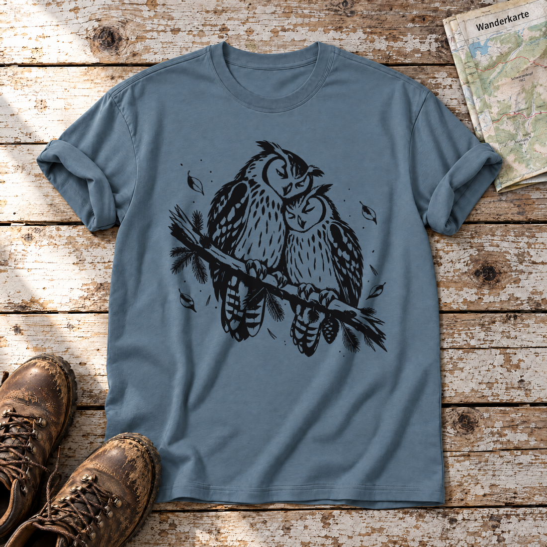 Uhupaar auf dem Fichtenast – T-Shirt Unisex in Steinblau, flach liegend auf alten Holzbrettern mit Wanderschuhen und Wanderkarte.