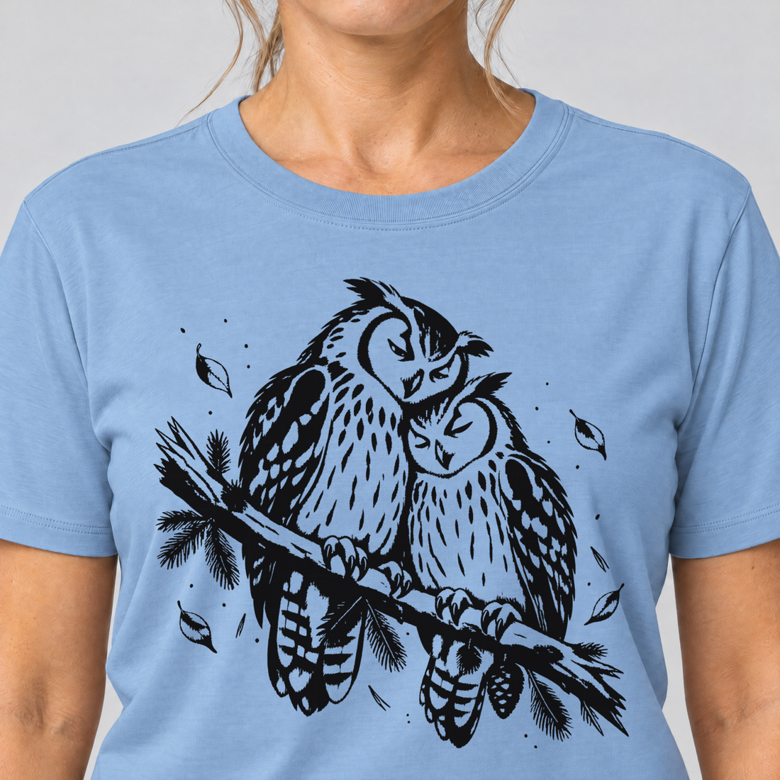 Nahaufnahme des Drucks: Uhupaar auf dem Fichtenast – T-Shirt Unisex in Himmelblau, von einer Frau getragen
