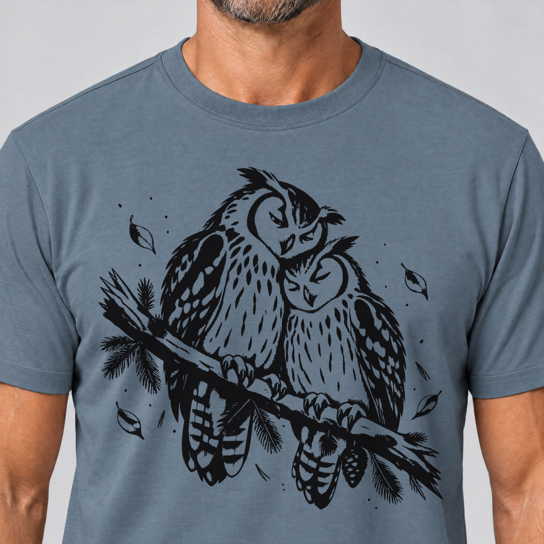 Nahaufnahme des Drucks: Uhupaar auf dem Fichtenast – T-Shirt Unisex in Steinblau, von einem Mann getragen