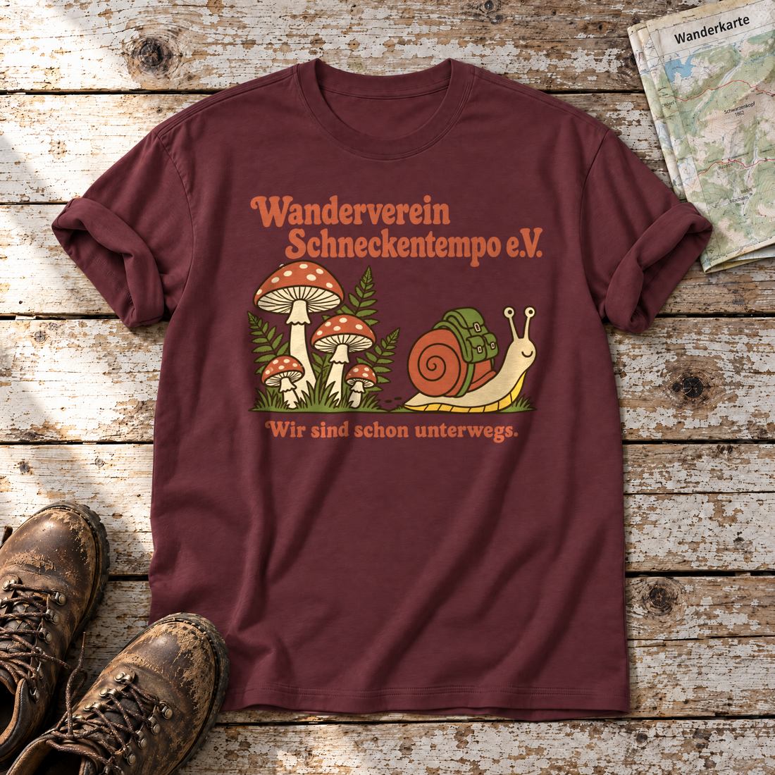 Wanderverein Schneckentempo – T-Shirt Unisex in Bordeaux, flach liegend auf alten Holzbrettern mit Wanderschuhen und Wanderkarte.