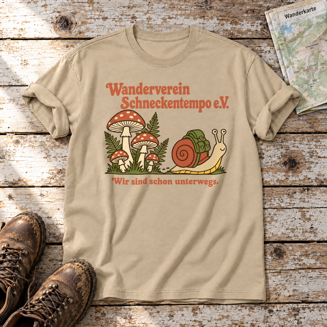 Wanderverein Schneckentempo – T-Shirt Unisex in Sand, flach liegend auf alten Holzbrettern mit Wanderschuhen und Wanderkarte.