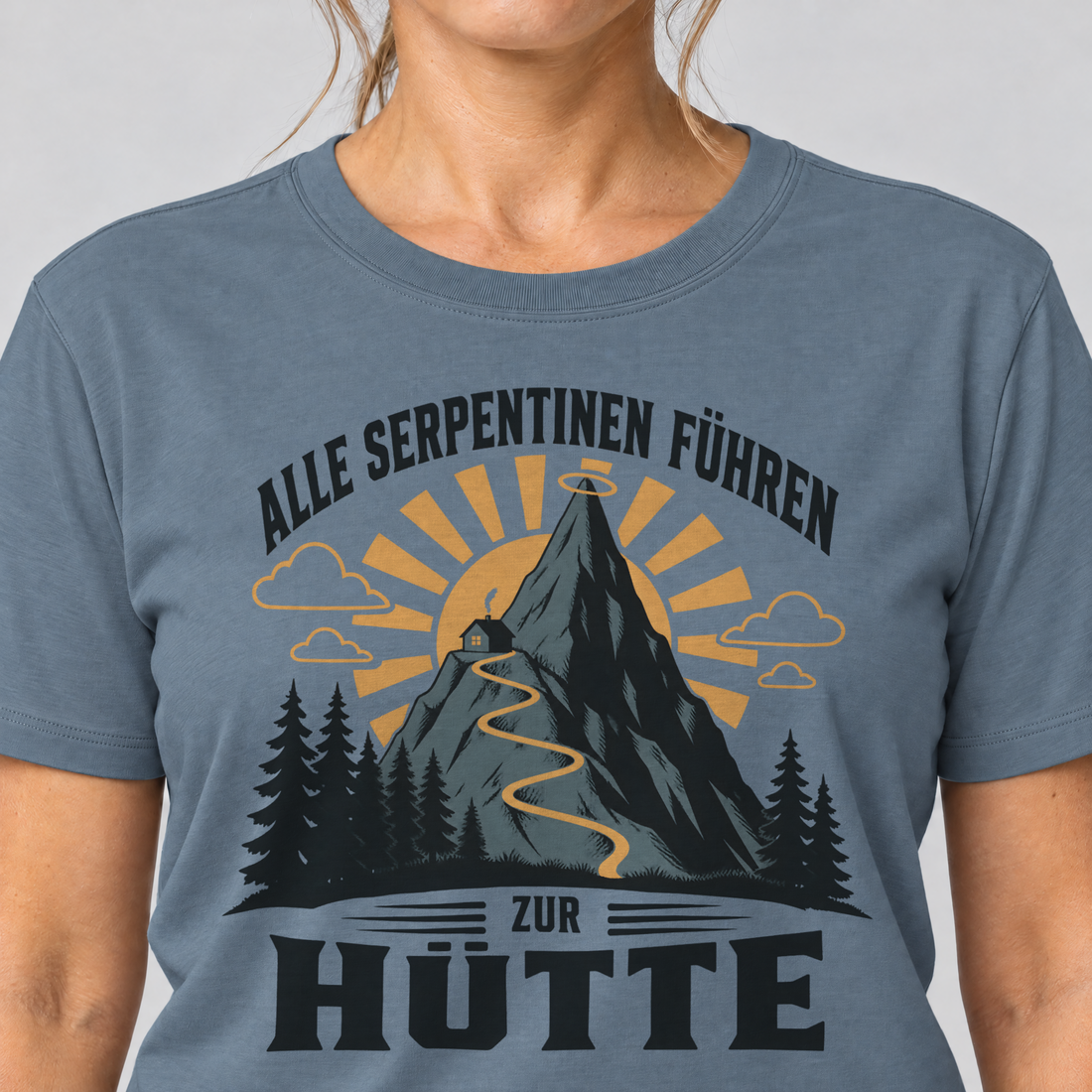 Nahaufnahme des Drucks: Alle Serpentinen führen zur Hütte – T-Shirt Unisex in Steinblau, von einer Frau getragen